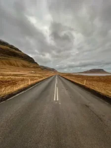 Long straight road through rugged landscape with mountains and dramatic cloudy sky
